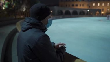 Kilitlenme teması yeni yıl tatili. Eğlence ve spor merkezleri kapandı. Noel tatilinde kapalı buz pateni pistinin yanında maske takan üzgün bir adam. Noel buz pateni pisti süslenmiş Noel ağacı boş
