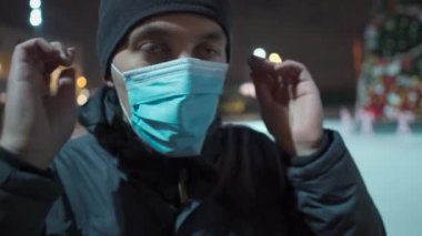Kilitlenme teması yeni yıl tatili. Eğlence ve spor merkezleri kapandı. Noel tatilinde kapalı buz pateni pistinin yanında maske takan üzgün bir adam. Noel buz pateni pisti süslenmiş Noel ağacı boş