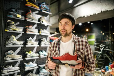 Satıcı, müşteriye açık hava mağazasında yürüyüş ayakkabısı seçimi konusunda tavsiye veriyor. Erkek turist dükkânı sahibi müşterilere yürüyüş botları denerken yardım ediyor. Genç satıcı kendinden emin bir şekilde dağ botu sunar. Sat, sat.