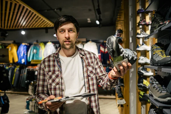 バイヤーにハイキングブーツを提示屋外店で白人男性セールスマンコンサルタント スポーツストアの営業担当者は 買い物客がハイキングブーツを選択するのに役立ちます スポーツ用品店の売り手 — ストック写真