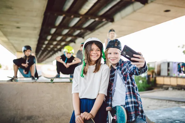 Twee tienermeisjes die een selfie foto nemen op een smartphone in een skatepark. Vriendschapsconcept. Kinderen maken social media content via de telefoon terwijl ze poseren voor de camera op een skate park helling — Stockfoto