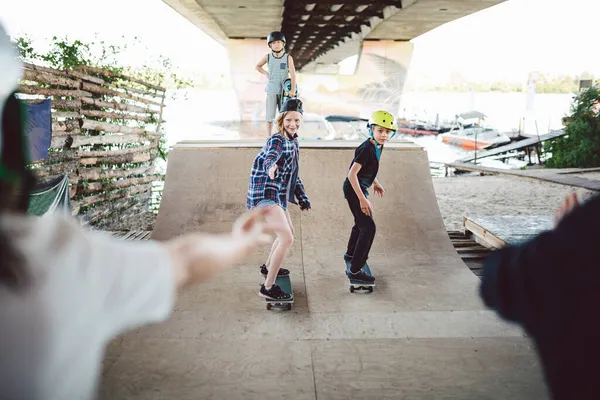 Vrienden skateboarders doen trucs tijdens het rollen op halve pipe in skate park. Sport, kinderen en buitenactiviteiten in het extreme park. Gelukkige kinderen op skateboards op de helling. Jonge skateboarders in het skatepark — Stockfoto