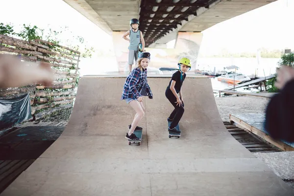 Jongens meisjes vrienden hebben plezier samen huilen tijdens skateboarden training, paardrijden en het doen van trucs op halve pijp in skate park. Jeugd, saamhorigheid en vriendschap concept. Sportclub voor kinderen — Stockfoto