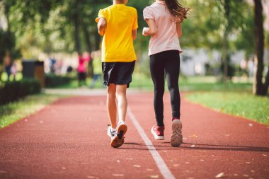 Stadyumun arka manzarasında koşan iki çocuğun spor ayakkabılarıyla bacakları yakın plan. Oğlan ve kız parkta koşuyor. Beden eğitimi sınıfındaki öğrenciler stadyumun etrafında koşuyorlar.