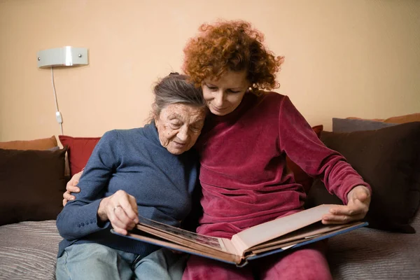 老妇人和她的成年女儿一起在客厅的沙发上看相册 兴高采烈地谈论着回忆 与父母共度的周末 家庭日 感恩节 妈妈的假期 — 图库照片