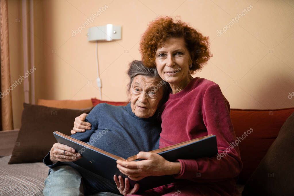Señoras de edad positiva mirando fotos del álbum sofá sentado en casa