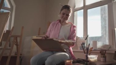 Sanat atölyesinde tuvale resim yapan hoş bir kadın. Ressam resim yaratıyor. Sanat okulu ya da stüdyo. Boya, fırça ve sehpayla çalış. Hobi ve eğlence konsepti. Çalışma alanındaki kadın ressam