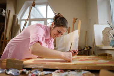 Sanat atölyesinde tuvale resim yapan hoş bir kadın. Ressam resim yaratıyor. Sanat okulu ya da stüdyo. Boya, fırça ve sehpayla çalış. Hobi ve eğlence konsepti. Çalışma alanındaki kadın ressam.