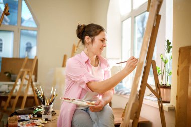 Sanat, yaratıcılık, hobi ve yaratıcı meslek kavramı. Yaratıcılığı canlandırmak. Resim stüdyosunda resim yapan bir kadın. Atölyede resim yapan çekici bir kadın sanatçı. Kadın hobisi, aktivite, meslek.
