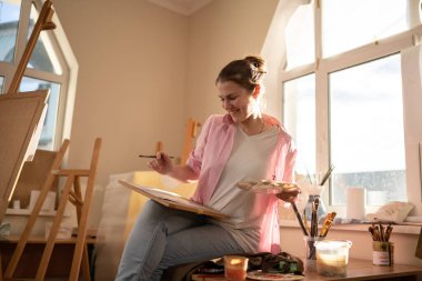 Sanat, yaratıcılık, hobi ve yaratıcı meslek kavramı. Yaratıcılığı canlandırmak. Resim stüdyosunda resim yapan bir kadın. Atölyede resim yapan çekici bir kadın sanatçı. Kadın hobisi, aktivite, meslek.