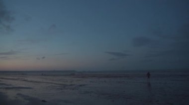 Atlantik Okyanusu 'ndaki gelgitten sonra, kuzey Fransa' da, Britanya Bölgesi 'nde günbatımında turist kıyı boyunca yürür. Ebb, Brittany sahilinde. Manzaralı kumsal ve deniz yansıması