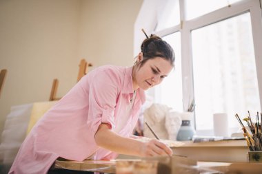 Sanat atölyesinde tuvale resim yapan hoş bir kadın. Ressam resim yaratıyor. Sanat okulu ya da stüdyo. Boya, fırça ve sehpayla çalış. Hobi ve eğlence konsepti. Çalışma alanındaki kadın ressam.