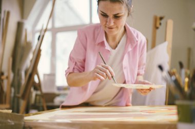Sanat atölyesinde tuvale resim yapan hoş bir kadın. Ressam resim yaratıyor. Sanat okulu ya da stüdyo. Boya, fırça ve sehpayla çalış. Hobi ve eğlence konsepti. Çalışma alanındaki kadın ressam.