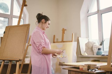 Sanat, yaratıcılık, hobi ve yaratıcı meslek kavramı. Yaratıcılığı canlandırmak. Resim stüdyosunda resim yapan bir kadın. Atölyede resim yapan çekici bir kadın sanatçı. Kadın hobisi, aktivite, meslek.