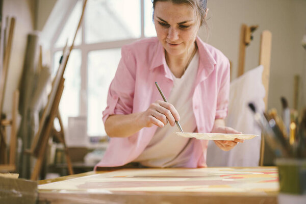 Милая женщина рисует на холсте в художественной мастерской. Художник создает картину. Школа искусств или студия. Работа с красками, кисточками и мольбертом. Концепция хобби и отдыха. Художница на рабочем месте.
