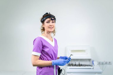 Mesleki tıp endüstrisi. Hastanın muayenesinden önce kadın KBB doktorunun portresi. Hastanedeki ENT uygulaması için tıbbi ekipman ve aletlerle parlak renkli üniformalı bir doktor..