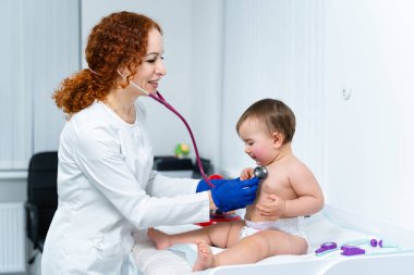 Pediyatrist doktor konsepti. Çocuklar için tıbbi bakım. Bir yaşındaki kız bebek klinikteki kadın çocuk doktoru tarafından muayene edildi. Sağlık kontrolü için çocuk doktoru ziyaret ediyor. Doktor küçük hastayı muayene ediyor..