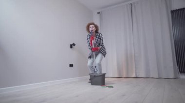 İnsanlar, ev işleri ve ev işleri konsepti. Koruyucu eldivenli mutlu yaşlı kadın yeni evine taşınmadan önce evde yerleri temizliyor ve dans ediyor. Ev idaresinden hoşlanan heyecanlı kadın