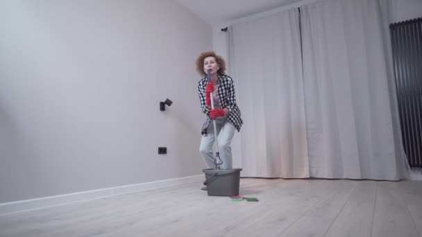 People, housework and housekeeping concept. Happy senior woman in protective gloves cleans floor and dances at home in empty apartment before moving to new home. Excited woman enjoying housekeeping — Stock Video