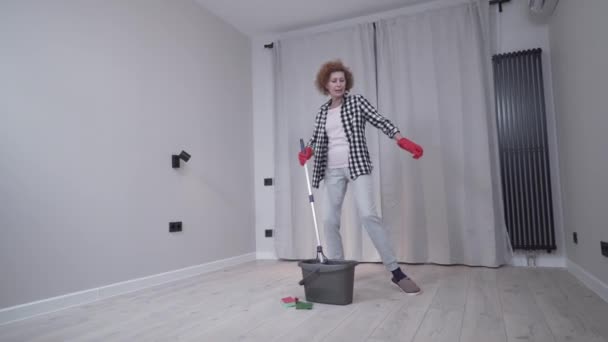 Jolly aufgeregt reife Frau genießen Putzen Haus, sie tanzt beim Waschen Boden. Glückliche ältere Frau, die es genießt, Fußböden zu putzen, bevor sie in eine neue Wohnung zieht. Hauswirtschaftskonzept — Stockvideo