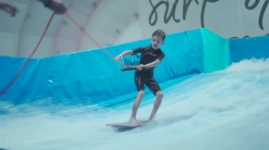 Çocuklar için kapalı sörf kulübü. Tema aktif eğlence ve su üzerinde ekstrem spor. Öğrenci ve koç dalga simülatöründe sörf eğitimi alıyor. Su parkında sörf tahtası.