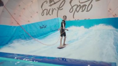 Çocuklar için kapalı sörf kulübü. Tema aktif eğlence ve su üzerinde ekstrem spor. Öğrenci ve koç dalga simülatöründe sörf eğitimi alıyor. Su parkında sörf tahtası.