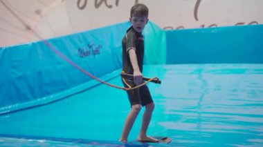 Su sporu aktivitesi, denge konsepti. Küçük sporcu ev içinde sörf yapmaktan hoşlanıyor. Gençler spor kompleksinde simülatörde dalgalarda sörf yapıyor. Sörf koçu ve öğrenci dalga simülatöründe toplandı