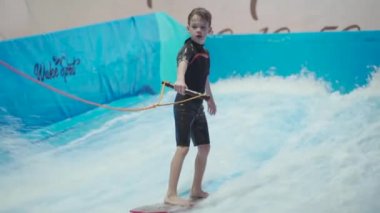 Çocuklar için kapalı sörf kulübü. Tema aktif eğlence ve su üzerinde ekstrem spor. Öğrenci ve koç dalga simülatöründe sörf eğitimi alıyor. Su parkında sörf tahtası.