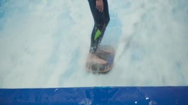 Su sporu aktivitesi, denge konsepti. Küçük sporcu ev içinde sörf yapmaktan hoşlanıyor. Gençler spor kompleksinde simülatörde dalgalarda sörf yapıyor. Sörf koçu ve öğrenci dalga simülatöründe toplandı