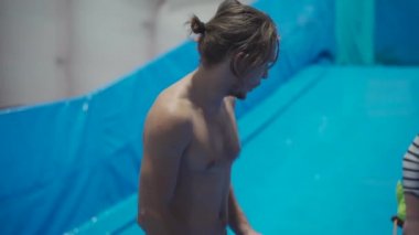 Su sporu aktivitesi, denge konsepti. Küçük sporcu ev içinde sörf yapmaktan hoşlanıyor. Gençler spor kompleksinde simülatörde dalgalarda sörf yapıyor. Sörf koçu ve öğrenci dalga simülatöründe toplandı