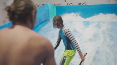 Çocuklar için kapalı sörf kulübü. Tema aktif eğlence ve su üzerinde ekstrem spor. Öğrenci ve koç dalga simülatöründe sörf eğitimi alıyor. Su parkında sörf tahtası.