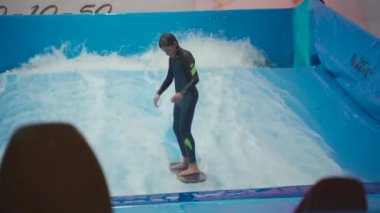 Su sporu aktivitesi, denge konsepti. Küçük sporcu ev içinde sörf yapmaktan hoşlanıyor. Gençler spor kompleksinde simülatörde dalgalarda sörf yapıyor. Sörf koçu ve öğrenci dalga simülatöründe toplandı
