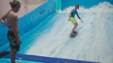 Çocuklar için kapalı sörf kulübü. Tema aktif eğlence ve su üzerinde ekstrem spor. Öğrenci ve koç dalga simülatöründe sörf eğitimi alıyor. Su parkında sörf tahtası.