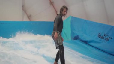 Su sporu aktivitesi, denge konsepti. Küçük sporcu ev içinde sörf yapmaktan hoşlanıyor. Gençler spor kompleksinde simülatörde dalgalarda sörf yapıyor. Sörf koçu ve öğrenci dalga simülatöründe toplandı