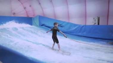 Su sporu aktivitesi, denge konsepti. Küçük sporcu ev içinde sörf yapmaktan hoşlanıyor. Gençler spor kompleksinde simülatörde dalgalarda sörf yapıyor. Sörf koçu ve öğrenci dalga simülatöründe toplandı