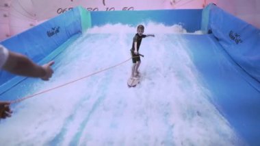 Çocuklar için kapalı sörf kulübü. Tema aktif eğlence ve su üzerinde ekstrem spor. Öğrenci ve koç dalga simülatöründe sörf eğitimi alıyor. Su parkında sörf tahtası.