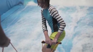 Su sporu aktivitesi, denge konsepti. Küçük sporcu ev içinde sörf yapmaktan hoşlanıyor. Gençler spor kompleksinde simülatörde dalgalarda sörf yapıyor. Sörf koçu ve öğrenci dalga simülatöründe toplandı