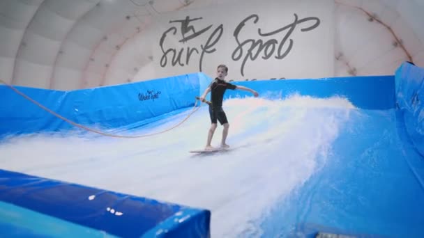 Wassersport, Gleichgewichtskonzept. Kleine Sportler genießen Indoor-Surfen. Teenager reitet Board auf Wellen auf Simulator in Sportkomplex. Surftrainer und Student im Wellensimulator — Stockvideo