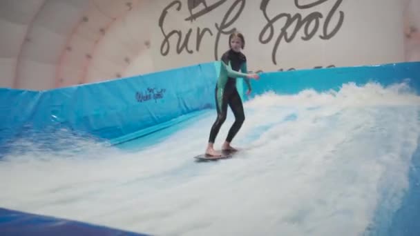 Clube de esportes de surf interior para crianças. Tema é recreação ativa e esportes radicais na água. Estudante e treinador em treinamento de surf em simulador de ondas. Adolescente prancha de surf no parque aquático — Vídeo de Stock