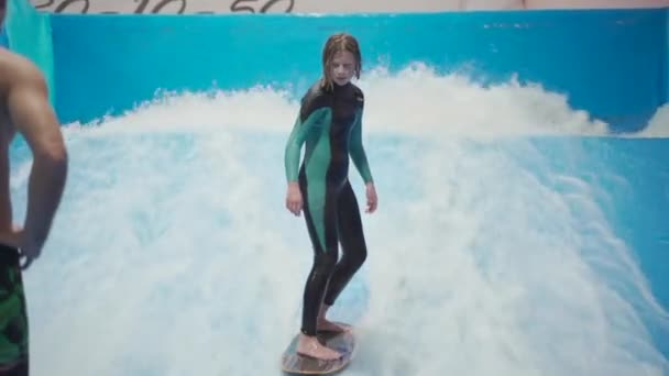 Adolescente está montando prancha de surf no simulador de ondas dentro de casa. Surfista jovem durante o treino em ondas geradas. Actividades desportivas aquáticas. Surfista garoto gosta de surfar no imitador de surf indoor. Treinamento de surf — Vídeo de Stock