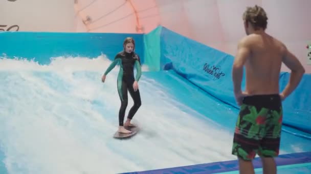 Barn och instruktör på Flow Rider inomhus surfing träningspass. Tonåring på vatten ombord utbildning på simulator våg inomhus. Ung surfare under träning på genererade vågor. Vattensporter — Stockvideo