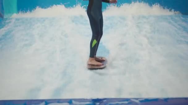 Barn og instruktør på Flow Rider indendørs surfing træning. Teenager på vand bord uddannelse på simulator bølge indendørs. Unge surfer under træning på genererede bølger. Vandsport – Stock-video