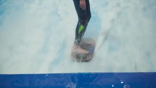 Actividad deportiva acuática, concepto de equilibrio. Pequeño atleta disfrutando del surf indoor. Los paseos adolescentes abordan olas en el simulador en el complejo deportivo. Entrenador de surf y estudiante en sesión en simulador de ola — Vídeo de stock