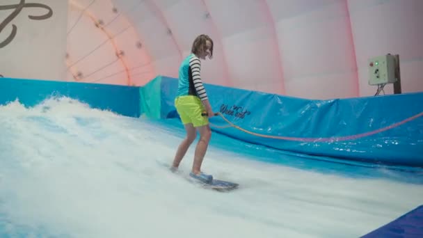 Dziecko i instruktor w Flow Rider trening surfingu krytego. Nastolatek na pokładzie wody szkolenia na symulator fali w pomieszczeniach. Młody surfer podczas treningu na generowanych falach. Sporty wodne — Wideo stockowe