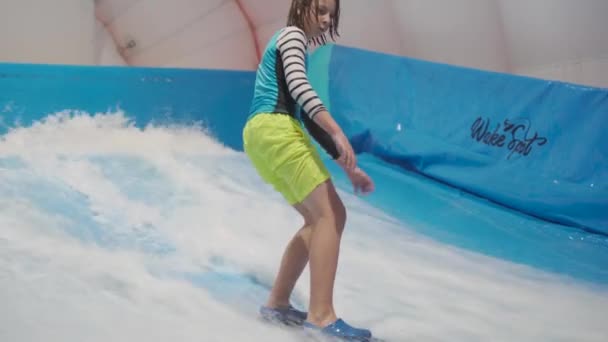 Tonåringen rider surfbräda på vågsimulator inomhus. Ung surfare under träning på genererade vågor. Vattensportaktivitet. Surfare kid njuta av surfing på inomhus surf imitator. Surfingträning — Stockvideo
