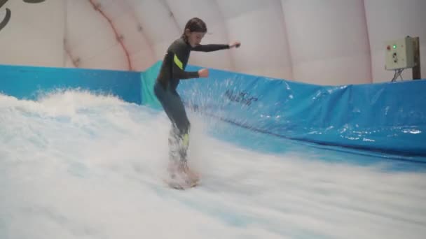 Dziecko i instruktor w Flow Rider trening surfingu krytego. Nastolatek na pokładzie wody szkolenia na symulator fali w pomieszczeniach. Młody surfer podczas treningu na generowanych falach. Sporty wodne — Wideo stockowe