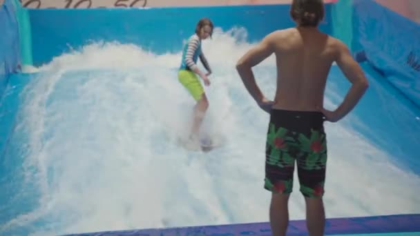 Dítě a instruktor na Flow Rider indoor surfing školení. Teenager na vodní desce školení na simulátoru vlny uvnitř. Mladý surfař během tréninku na generovaných vlnách. Vodní sporty — Stock video