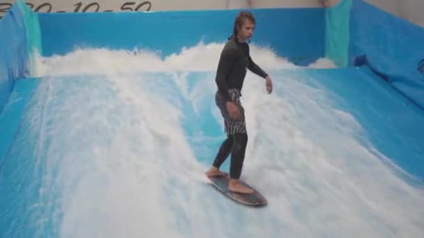 Teenager rider surf board på bølge simulator indendørs. Unge surfer under træning på genererede bølger. Vandsportsaktiviteter. Surfer kid nyde surfing på indendørs surf imitator. Surfing uddannelse – Stock-video