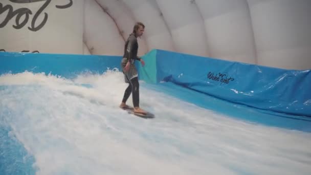 Kind en instructeur bij Flow Rider indoor surftraining. Tiener op waterboard training op simulator wave binnen. Jonge surfer tijdens de training op gegenereerde golven. Watersport — Stockvideo