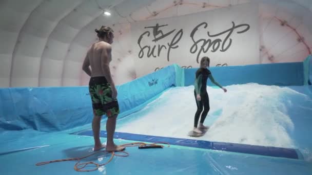 Barn og instruktør på Flow Rider indendørs surfing træning. Teenager på vand bord uddannelse på simulator bølge indendørs. Unge surfer under træning på genererede bølger. Vandsport – Stock-video